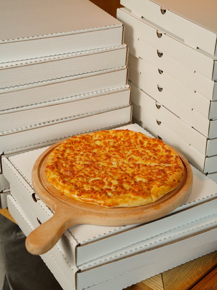 Appetizing cheese pizza on a wooden board atop a stack of delivery boxes, ready to serve.